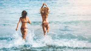Home Vrouw in felgekleurde mooiste bikini's op het strand met zonnebril en zonbruine teint